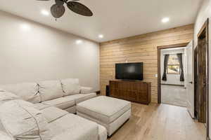Living room with light wood-style floors, wooden walls, recessed lighting, ceiling fan, and an accent wall