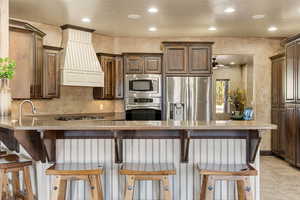Kitchen featuring a breakfast bar, stainless steel appliances, a peninsula, recessed lighting, and light stone countertops