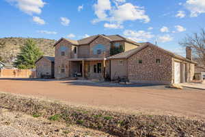 View of front facade featuring stone siding, covered porch, an attached garage, driveway, and stucco siding