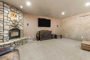 Living area featuring carpet, a stone fireplace, recessed lighting, and a textured wall