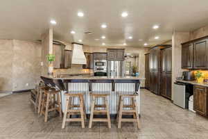 Kitchen with dark wood finish cabinetry, a kitchen bar, a peninsula, stainless steel appliances, and light stone countertops
