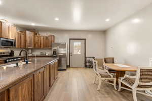 Kitchen featuring stainless steel appliances, light wood-style flooring, wood finish cabinetry, dark stone counters, and recessed lighting