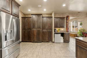 Kitchen with stainless steel fridge, dark wood finish cabinetry, recessed lighting, and light stone countertops