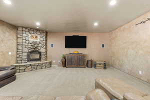 Living room with carpet, a stone fireplace, recessed lighting, and a textured wall