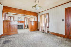 Unfurnished living room featuring wallpapered walls, carpet, a chandelier, a fireplace, and plenty of natural light