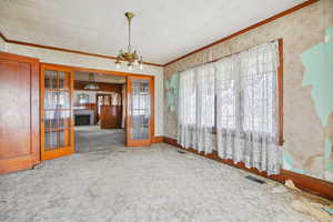Spare room featuring wallpapered walls, a fireplace, suspended lighting, carpet, and french doors