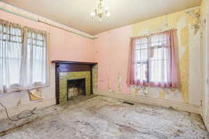 Unfurnished living room featuring a chandelier, healthy amount of natural light, and a fireplace with flush hearth