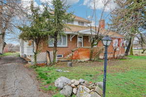 View of front of property featuring brick siding, roof with shingles, a front lawn, and a chimney