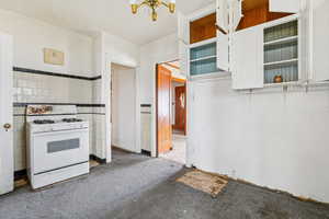Kitchen with a textured ceiling, white range with gas stovetop, tile walls, white cabinetry, and wainscoting