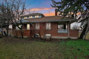 View of front facade with brick siding, a chimney, a yard, and covered porch