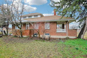 View of front of house featuring brick siding, covered porch, a chimney, roof with shingles, and a front lawn