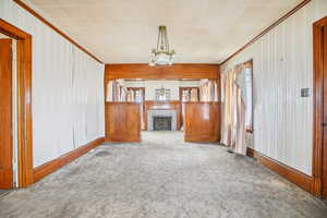 Unfurnished living room featuring crown molding, wallpapered walls, a tile fireplace, a chandelier, and carpet