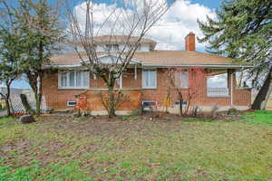 Back of property featuring brick siding, a chimney, a yard, and roof with shingles