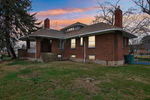 Rear view of house with a chimney, a lawn, brick siding, covered porch, and a shingled roof