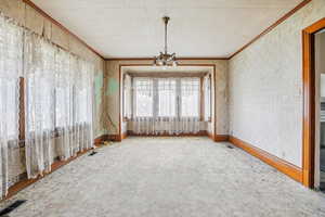 Spare room featuring suspended lighting, crown molding, and wallpapered walls