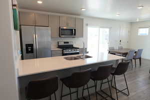 Kitchen with gray cabinets, stainless steel appliances, dark wood finished floors, a kitchen bar, and a peninsula