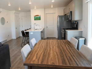 Kitchen with a breakfast bar area, gray cabinets, stainless steel appliances, dark wood-type flooring, and a peninsula