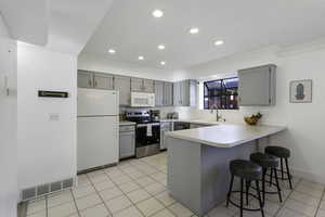 Kitchen featuring a peninsula, a kitchen breakfast bar, light countertops, white appliances, and gray cabinetry