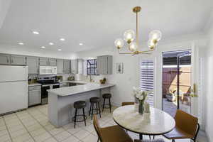 Kitchen with white appliances, gray cabinetry, a breakfast bar, light countertops, and a peninsula