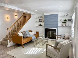 Living room with wood finished floors, a textured ceiling, a fireplace, crown molding, and recessed lighting