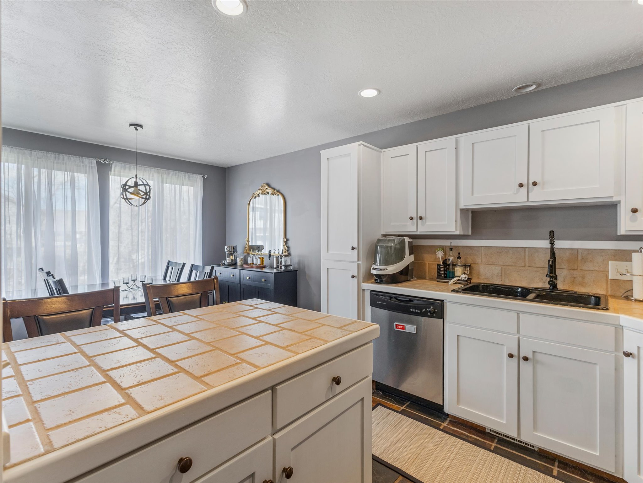 Kitchen with white cabinetry, dishwasher, pendant lighting, decorative backsplash, and a textured ceiling