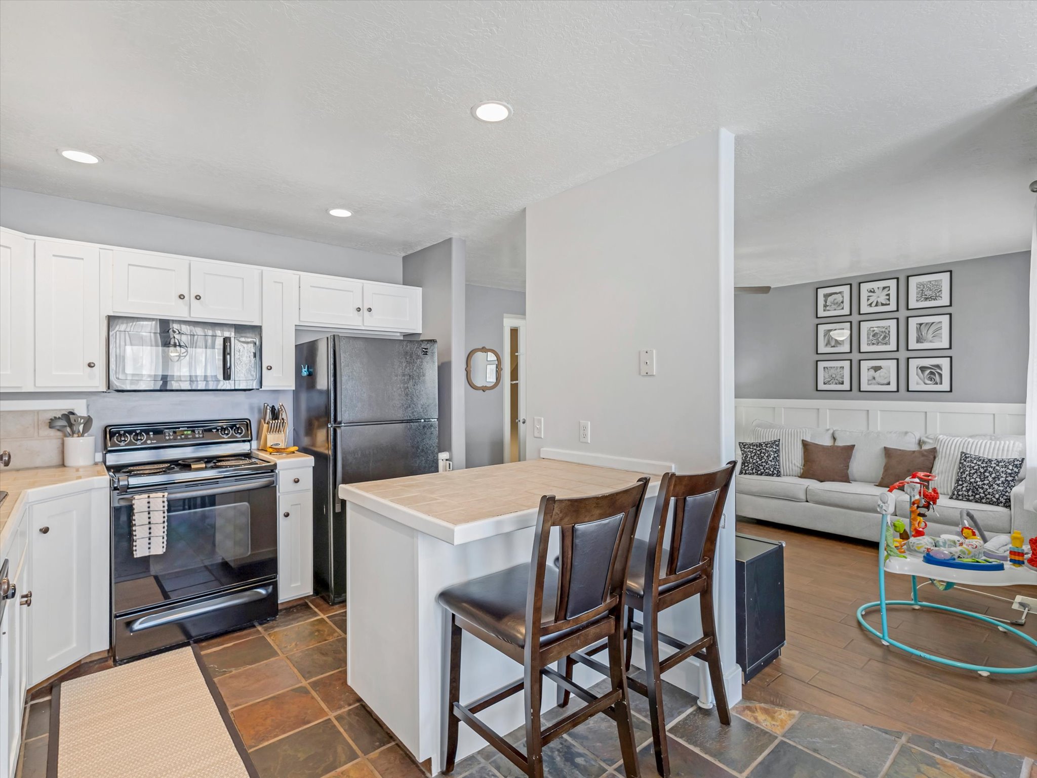Kitchen featuring black appliances, a kitchen breakfast bar, light countertops, white cabinetry, and a wainscoted wall
