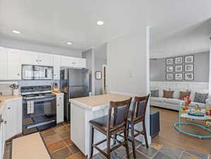 Kitchen featuring black appliances, a kitchen breakfast bar, light countertops, white cabinetry, and a wainscoted wall