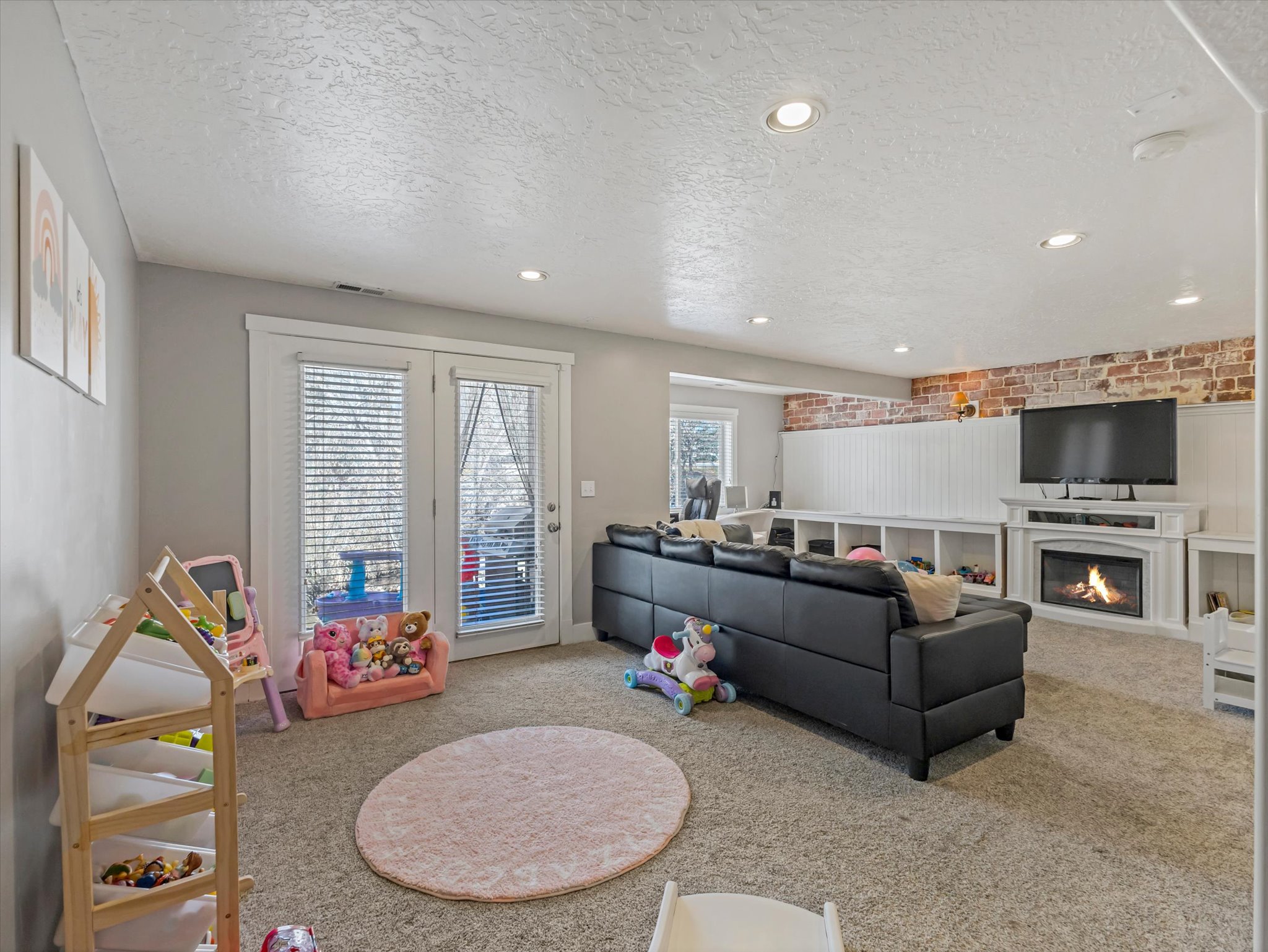 Carpeted living area featuring a textured ceiling, a warm lit fireplace, recessed lighting, and brick wall