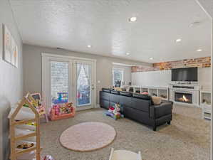 Carpeted living area featuring a textured ceiling, a warm lit fireplace, recessed lighting, and brick wall