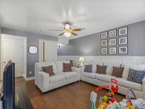 Living area with a ceiling fan, dark wood-style floors, and wainscoting