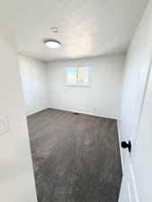 Unfurnished room featuring dark colored carpet and a textured ceiling