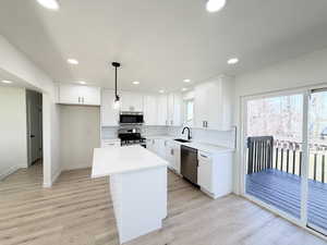 Kitchen with a center island, stainless steel appliances, white cabinets, light wood finished floors, and tasteful backsplash