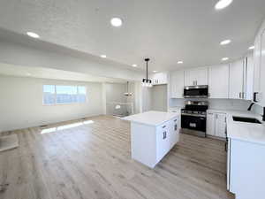 Kitchen featuring stainless steel appliances, open floor plan, a kitchen island, white cabinetry, and light stone counters