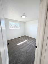 Unfurnished room with dark colored carpet and a textured ceiling