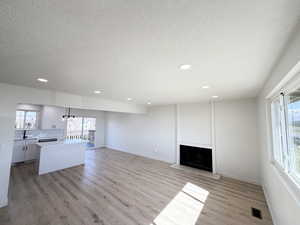 Unfurnished living room featuring healthy amount of natural light, a textured ceiling, a fireplace, light wood-style floors, and hanging lights