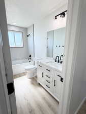 Bathroom with vanity, washtub / shower combination, light wood-style flooring, and a textured ceiling