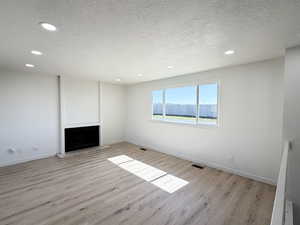 Unfurnished living room with a textured ceiling, recessed lighting, light wood-type flooring, and a fireplace with raised hearth
