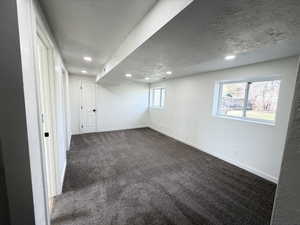 Basement featuring a textured wall, dark carpet, and recessed lighting