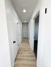 Hall featuring light wood finished floors, a textured ceiling, and recessed lighting