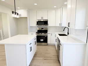 Kitchen featuring stainless steel appliances, a center island, white cabinets, light wood finished floors, and tasteful backsplash