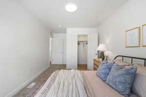 Bedroom with light colored carpet and a walk in closet