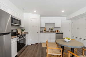 Kitchen with stainless steel appliances, dark wood finished floors, white cabinets, dark stone counters, and recessed lighting