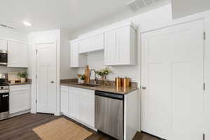 Kitchen with white cabinetry, stainless steel appliances, dark stone countertops, and dark wood finished floors