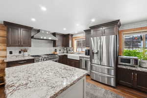 Kitchen with stainless steel appliances, dark wood finish cabinetry, light stone counters, dark wood-style flooring, and recessed lighting