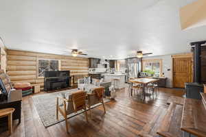 Living area featuring a wood stove, dark wood-style flooring, log walls, and ceiling fan
