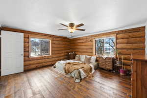 Bedroom featuring rustic walls, dark wood-style floors, ceiling fan, and a textured ceiling