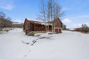 Snow covered back of property with log siding, stone siding, and a porch