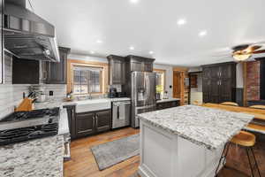 Kitchen with exhaust hood, light stone countertops, a breakfast bar area, dual tone cabinets, and light wood-type flooring