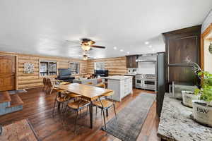 Dining room featuring dark wood-type flooring, log walls, ceiling fan, and recessed lighting