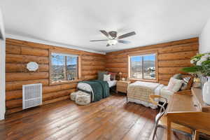 Bedroom featuring heating unit, hardwood / wood-style flooring, multiple windows, log walls, and ceiling fan